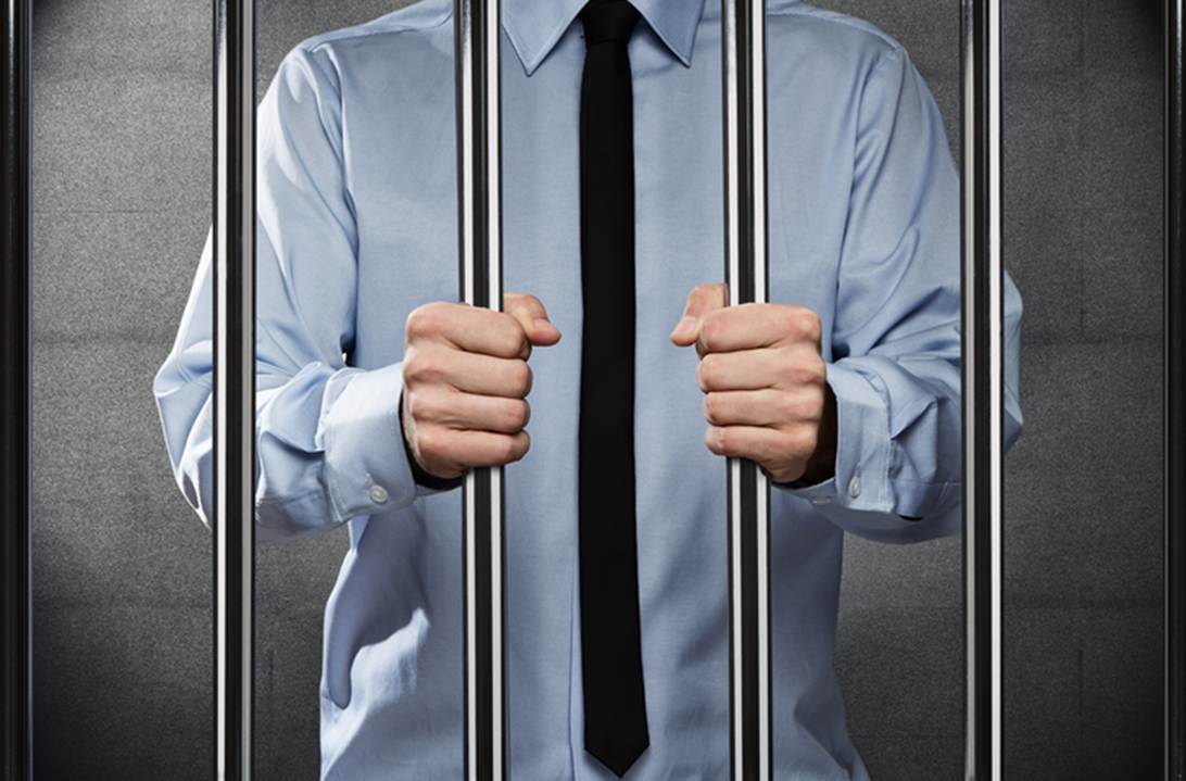 A man in a shirt and tie is behind bars. This image symbolizes the restraint of employee freedom, as mentioned in the surrounding text.